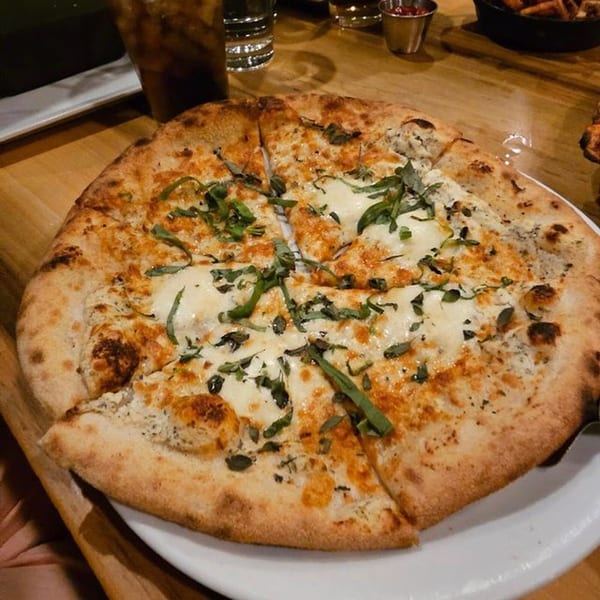 A Fox's Den white pizza with basil and cheese, sliced on a white plate.