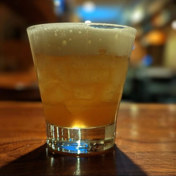 A foamy, amber-colored cocktail with ice sits on a wooden bar at Fox's Den.