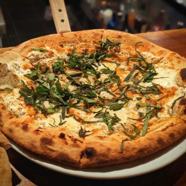 A Fox's Den white pizza with fresh basil, ricotta, and mozzarella cheese on a white plate.